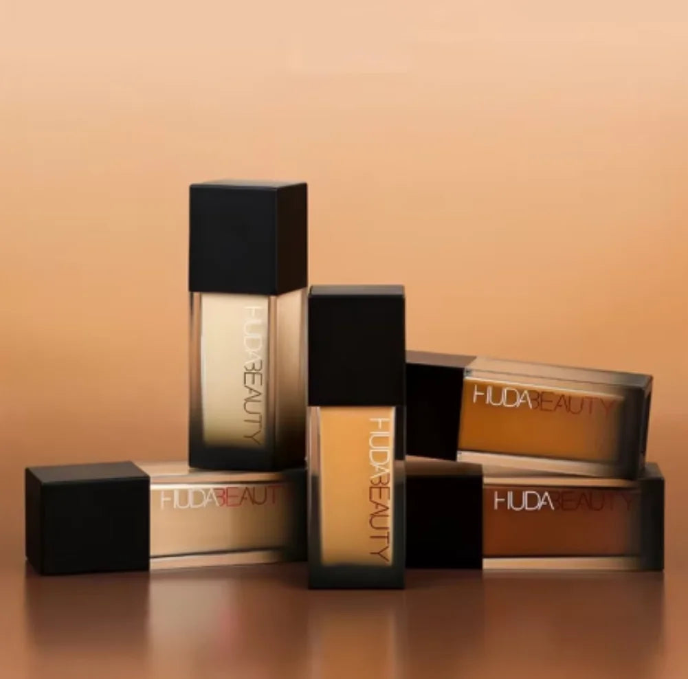 HUDA Flawless Liquid Foundation Matte Concealer bottles arranged on a gradient background.